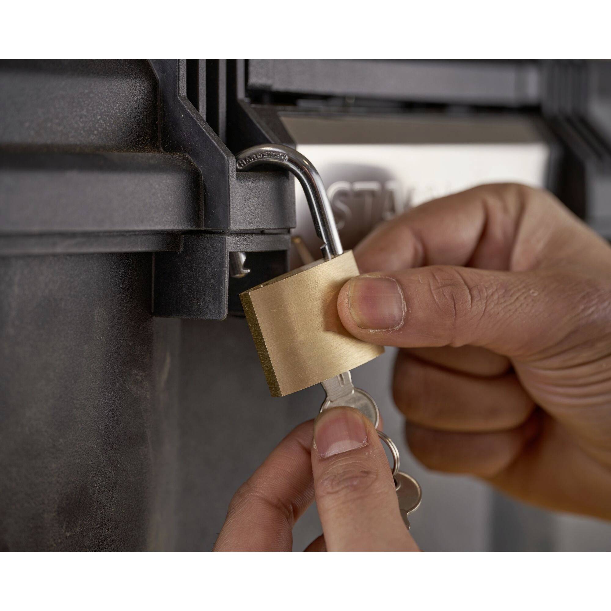 Une main déverrouille un cadenas sur un coffret métallique en insérant une clé dans la serrure.