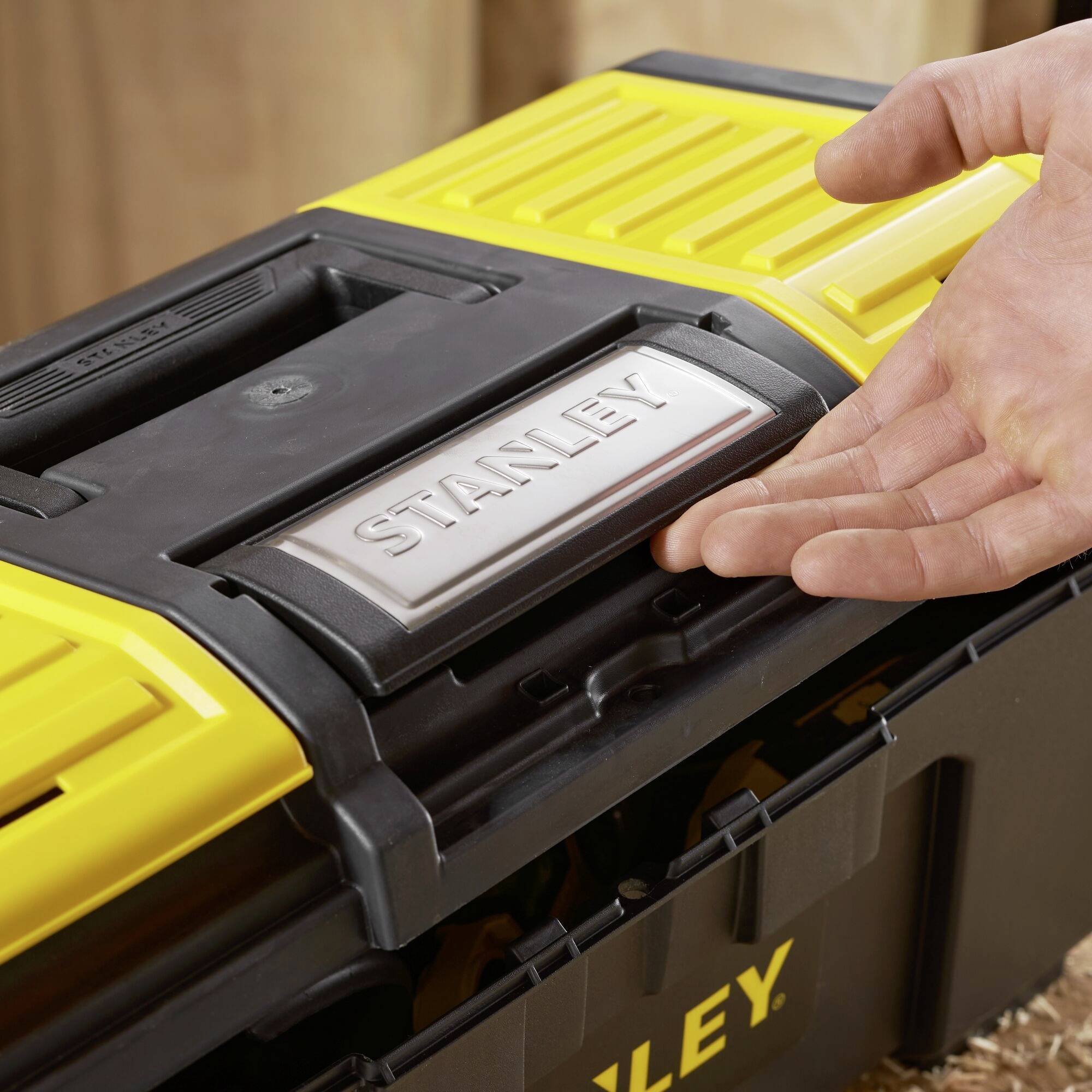 Une boîte à outils jaune avec une poignée noire et le logo 'STANLEY' est tenue sur une surface en bois.