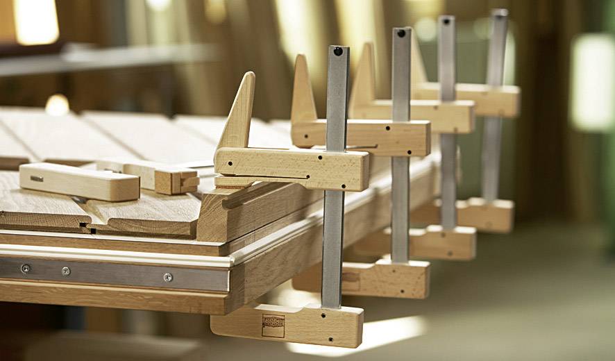 Plusieurs serre-joints en bois et en métal maintiennent fermement des planches sur une table dans un atelier de menuiserie de précision.