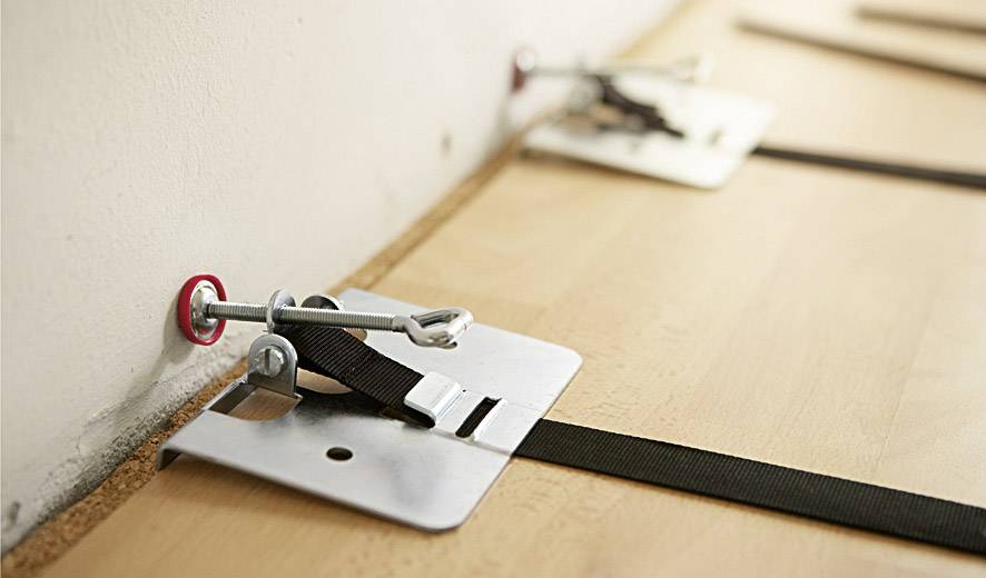 Des agrafes de fixation sécurisent un plancher en bois. Les agrafes sont attachées à des vis murales et maintiennent les planches de manière stable.