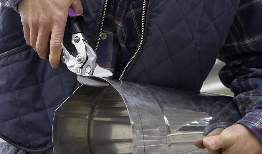 Une personne coupe un tube métallique à l'aide de cisailles métalliques. Les mains sont visibles, l'accent étant mis sur l'action de couper.