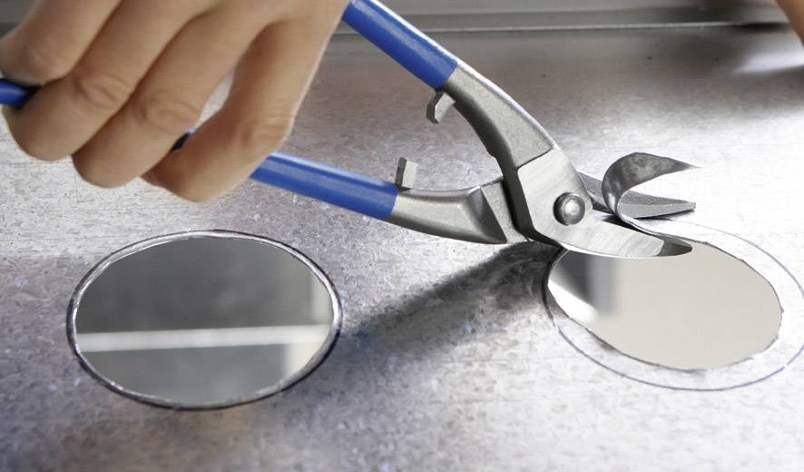 Une main découpe un cercle dans une tôle métallique à l'aide d'une pince.