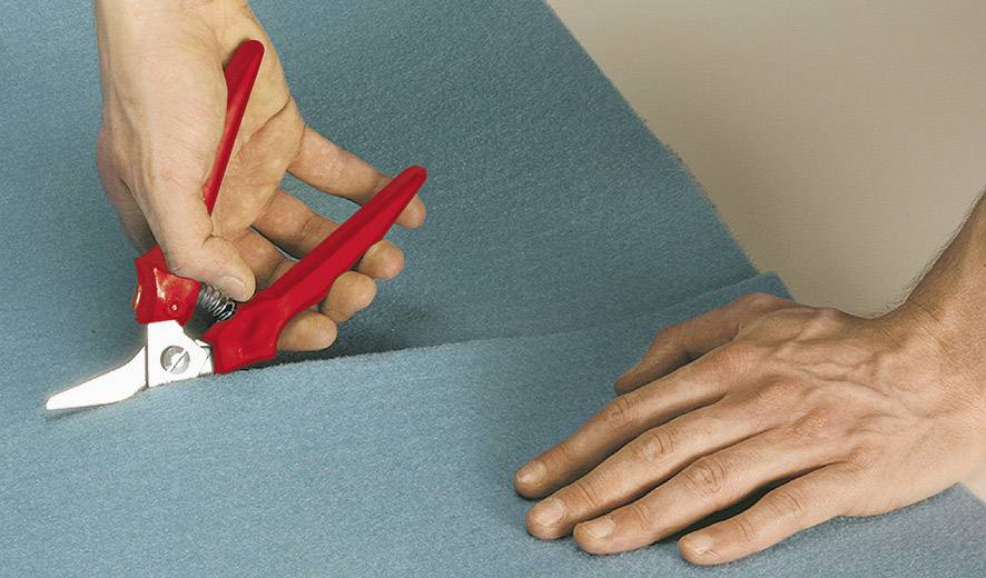 Deux mains travaillent avec des ciseaux rouges pour couper du tissu bleu.