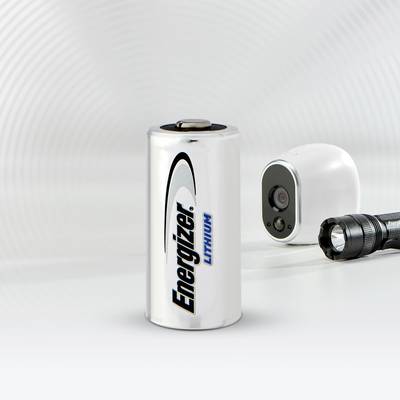 Pile de marque Energizer, placée à côté d'un petit appareil photo et d'une lampe de poche, sur un fond blanc.