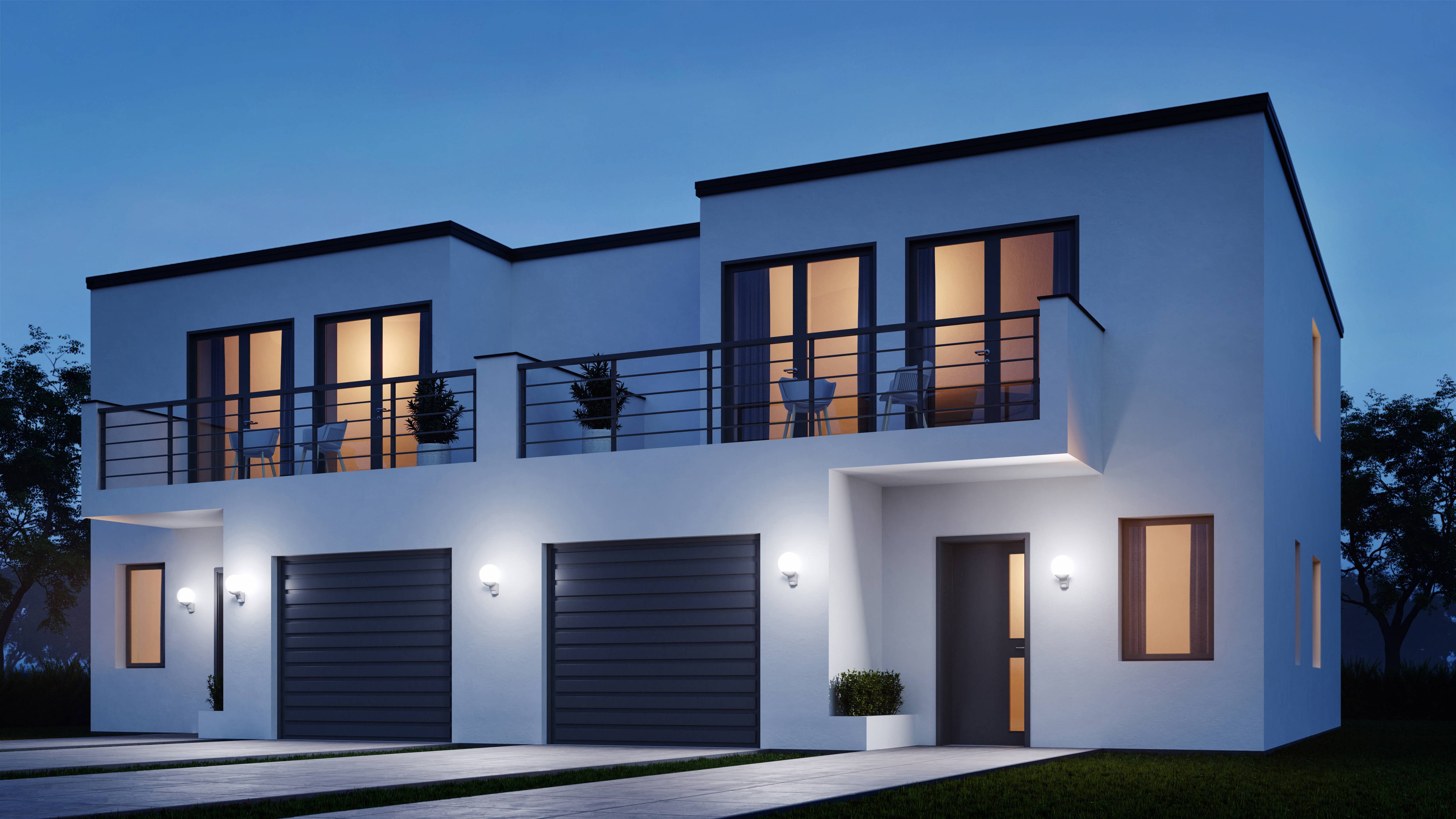 Maison moderne à deux étages le soir ; façade blanche, grandes fenêtres, balcons avec des plantes, double garage, éclairée au crépuscule.