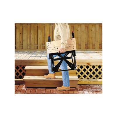 Une personne monte un tabouret pliant en bois et en métal le long d'un escalier en bois. À l'arrière-plan, on aperçoit une véranda en bois.