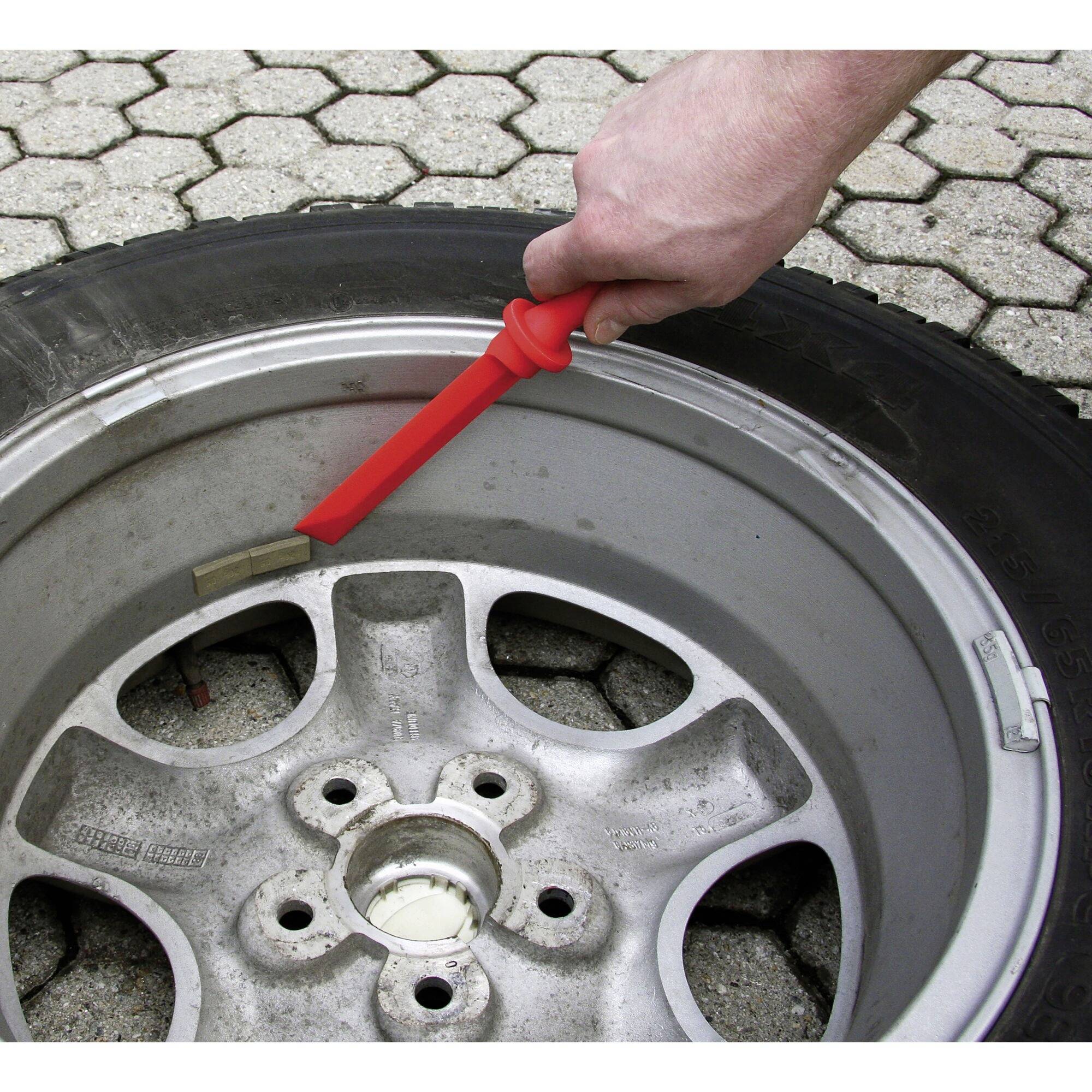 Une main pointe un marqueur rouge sur le bord d'un pneu de voiture endommagé sur un pavage en pierre.