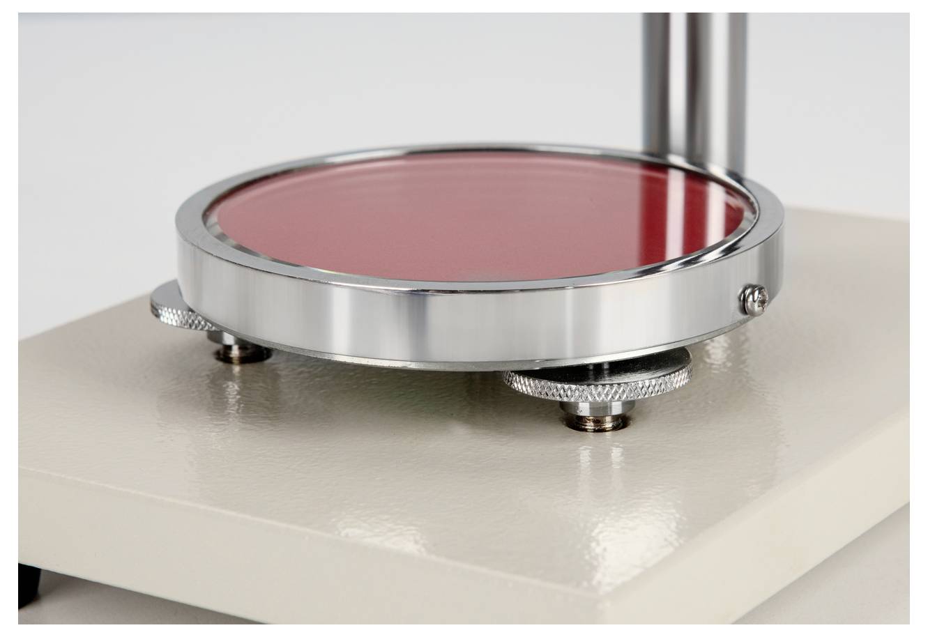 Un appareil de laboratoire rond en métal avec des pieds réglables et un disque rouge sur une base blanche.