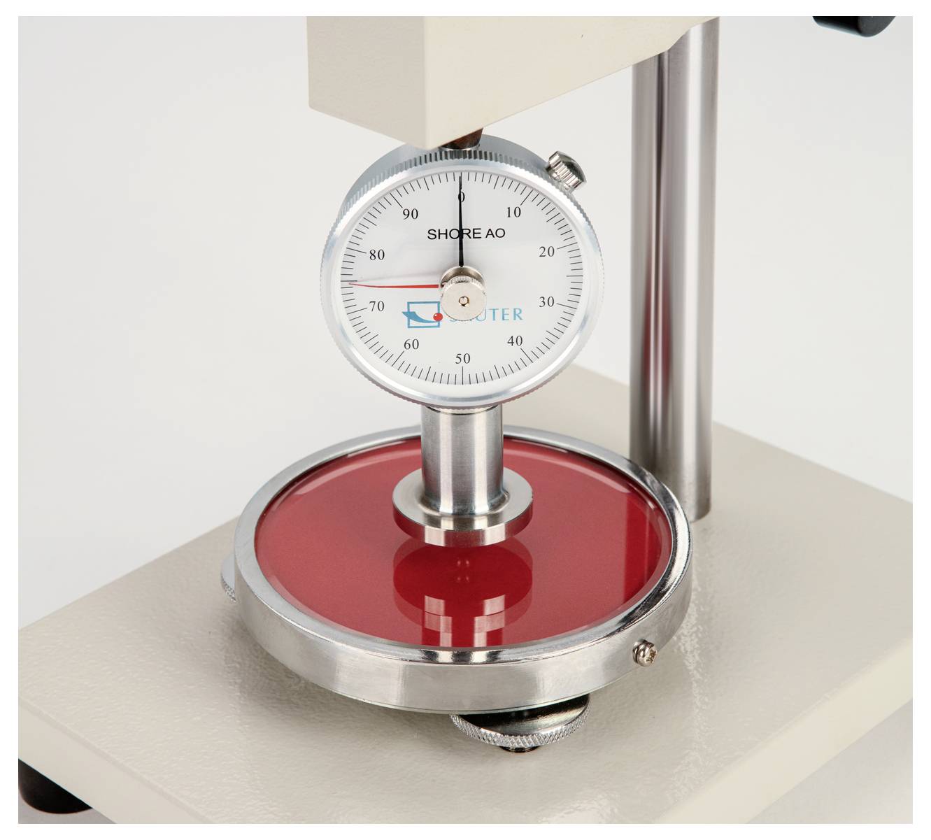 Un appareil de mesure de dureté avec un cadran rond indique le degré de dureté sur une surface rouge.