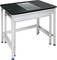 Une table à surface noire avec un insert rectangulaire transparent au centre. La table repose sur un châssis en métal argenté.