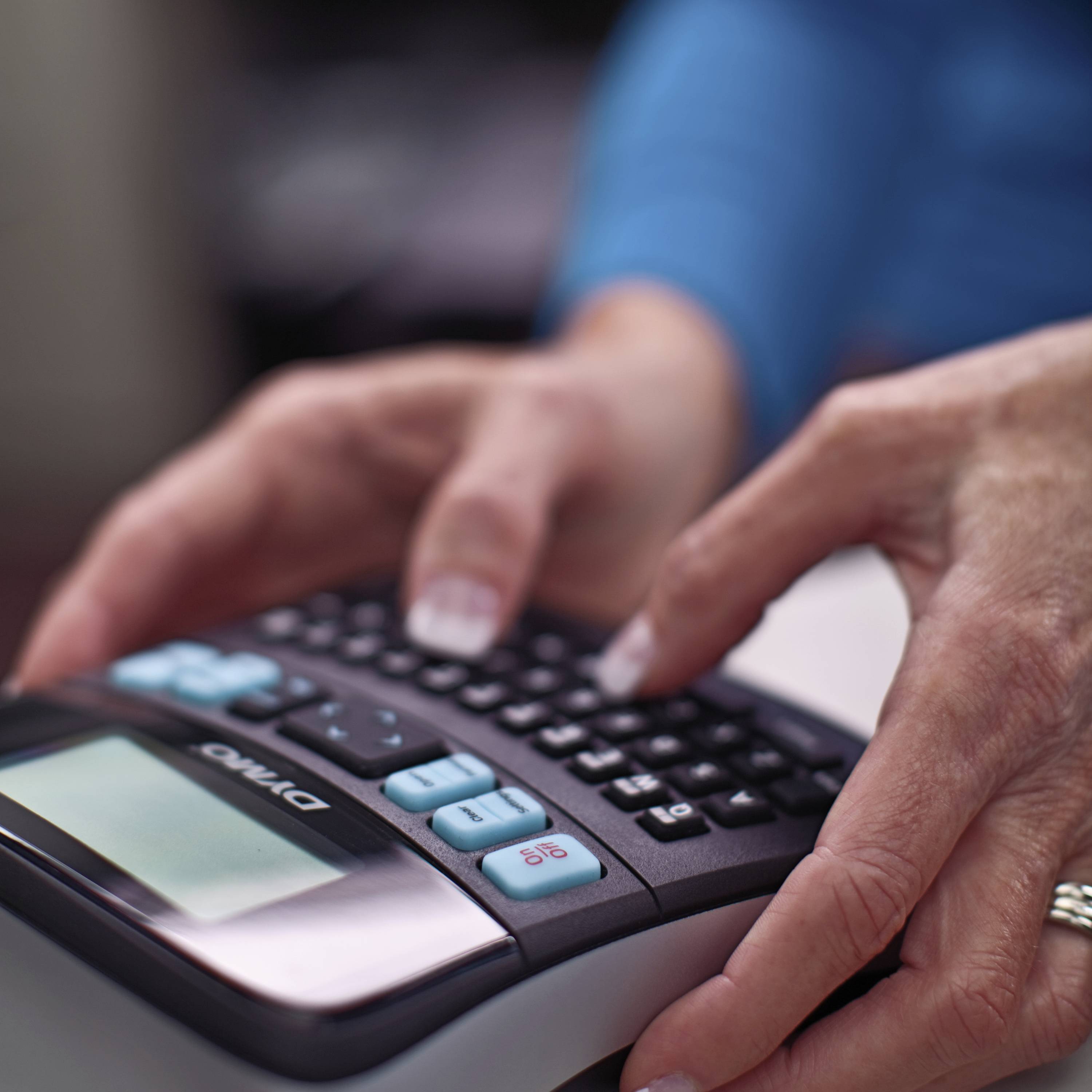 Une personne appuie sur les touches d'une calculatrice. Le focus est mis sur les mains qui actionnent les touches.