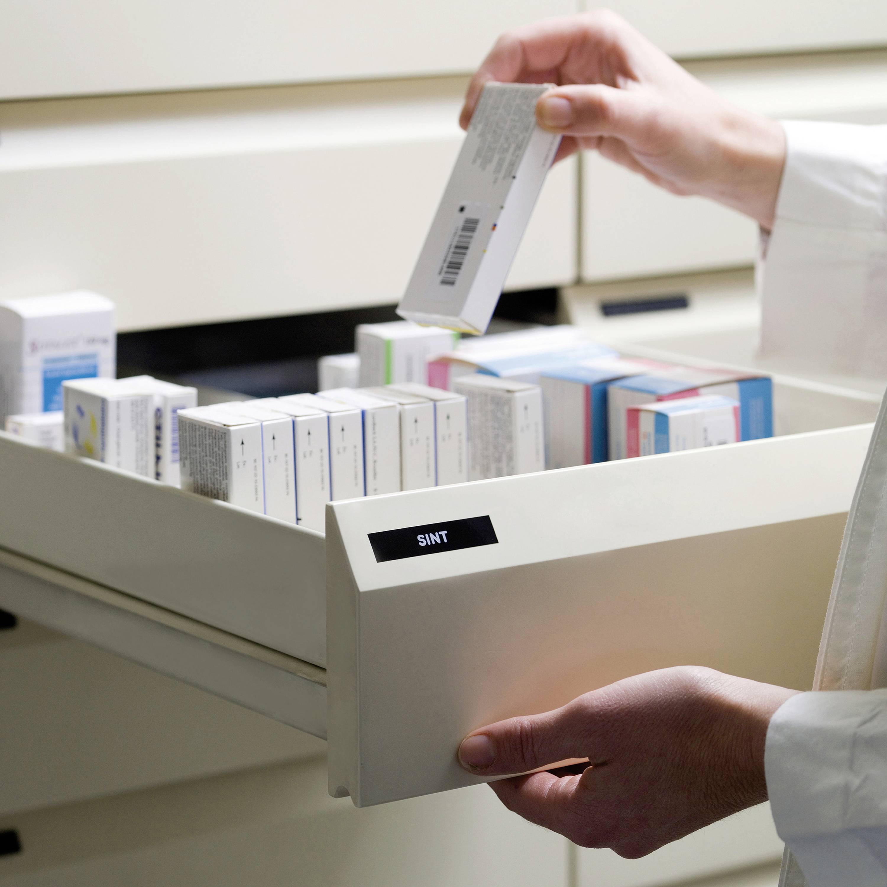 Une main prend une boîte de médicaments dans un tiroir ouvert rempli d'autres médicaments.