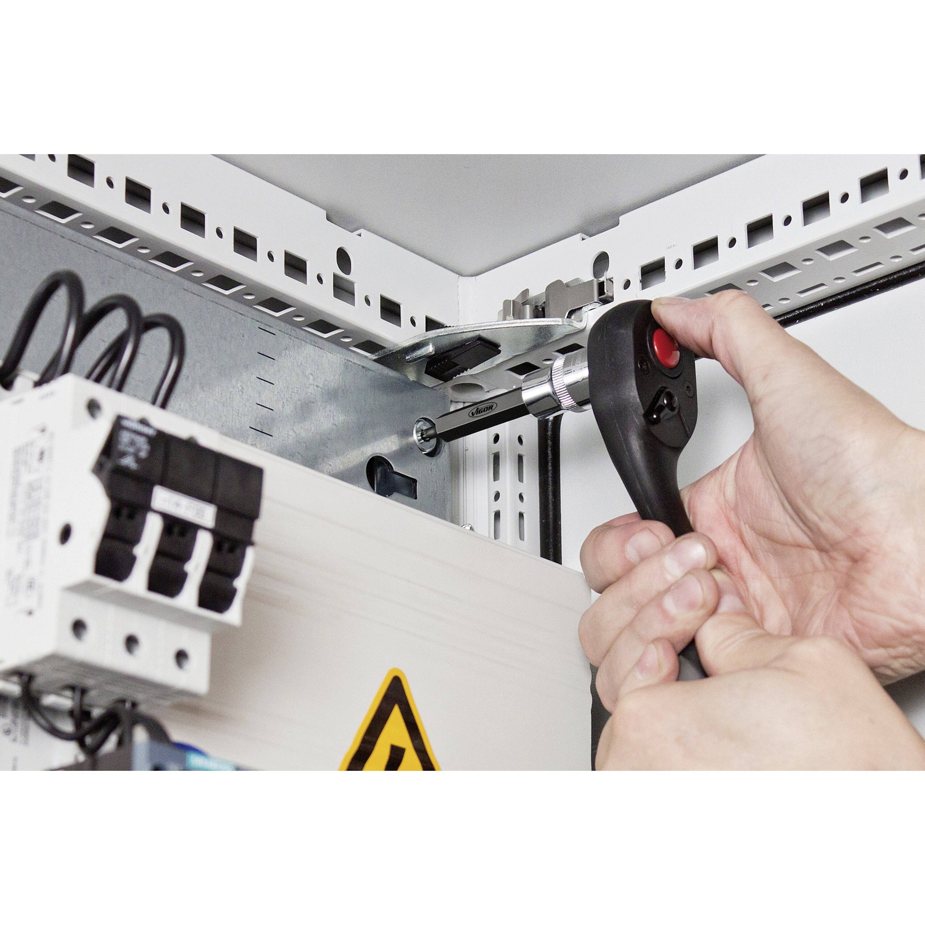 « Gros plan sur des mains utilisant une clé à cliquet pour serrer un boulon à l'intérieur d'un tableau électrique, illustrant un travail de maintenance. »