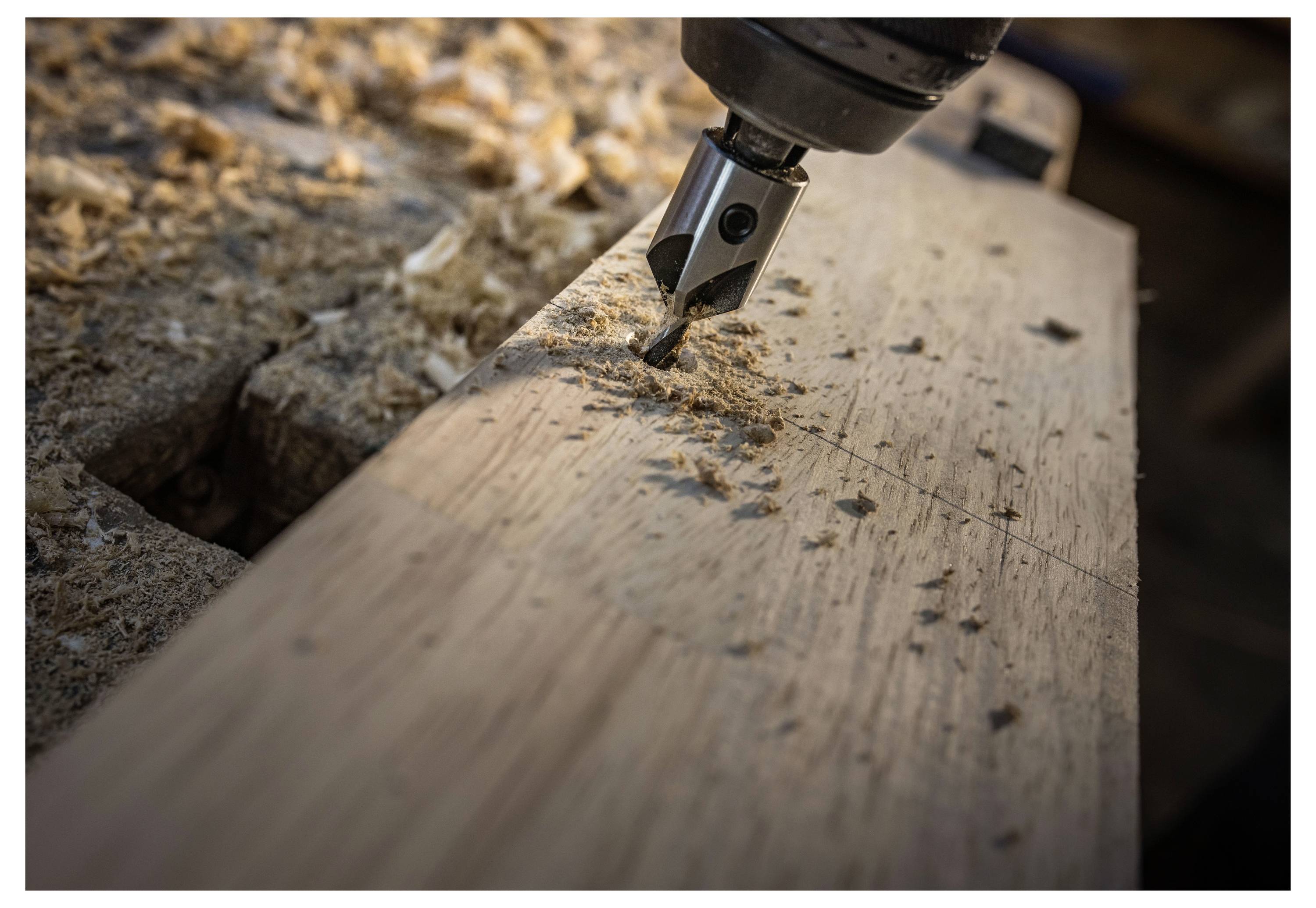 Gros plan d'une mèche de perceuse s'enfonçant dans une planche de bois, avec des copeaux de bois éparpillés autour du trou.