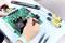 Une personne répare un circuit imprimé vert à l'aide d'outils sur une table.