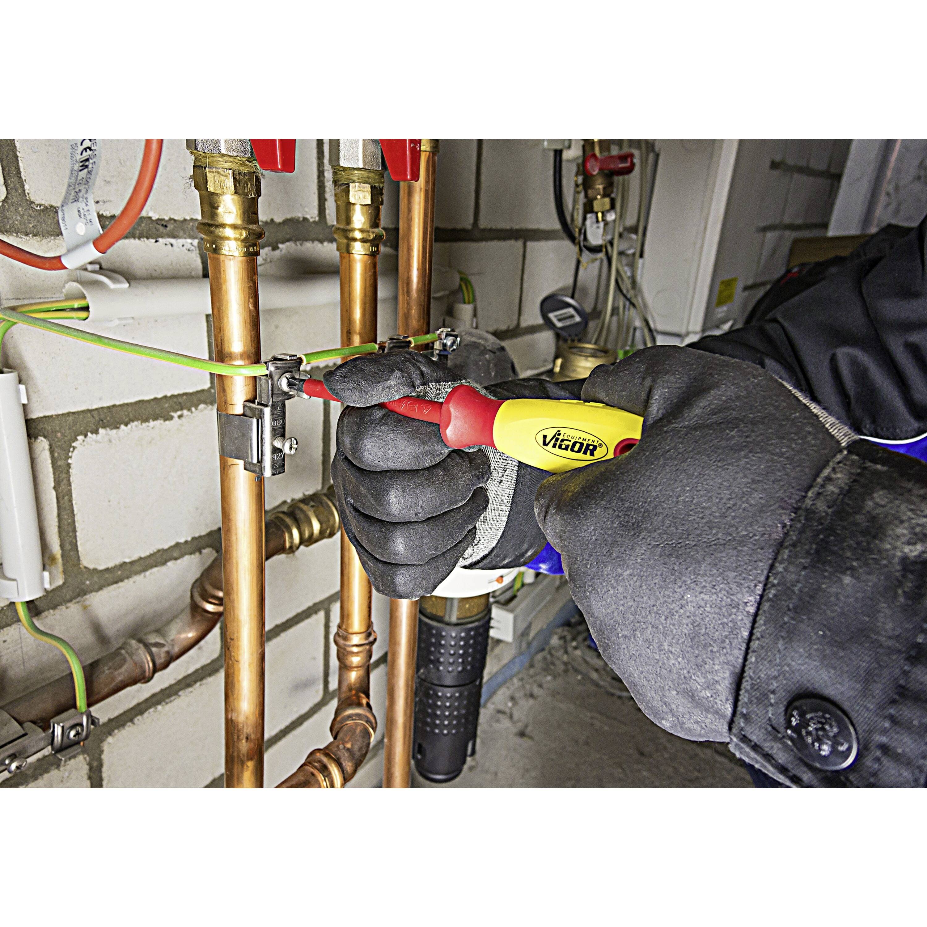 « Une personne portant des gants utilise un testeur de tension rouge et jaune sur un collier de serrage dans un environnement industriel. »