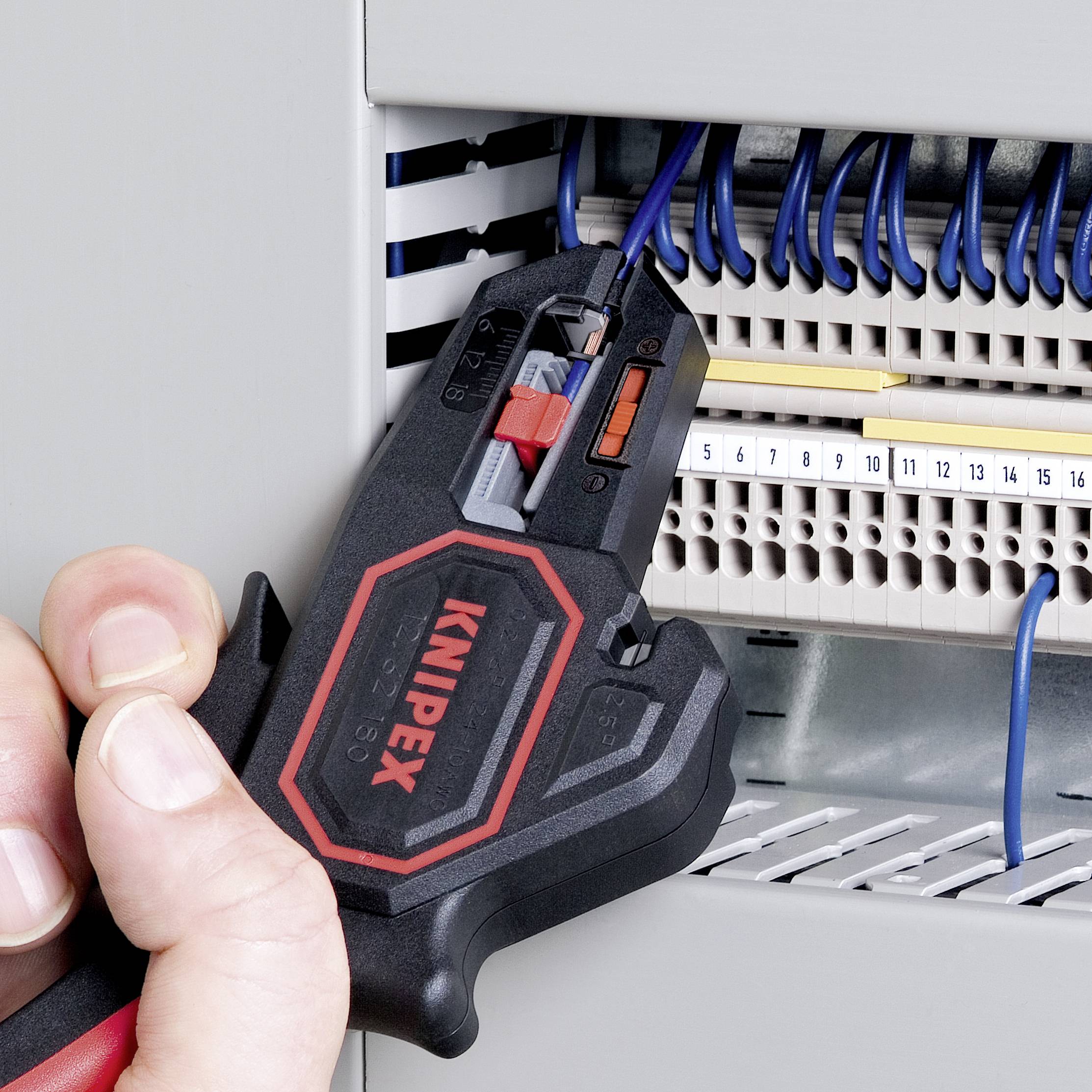 Un outil est utilisé pour travailler un câble dans un armoire électrique. À l'arrière-plan, on peut voir des câbles et des bornes de raccordement.