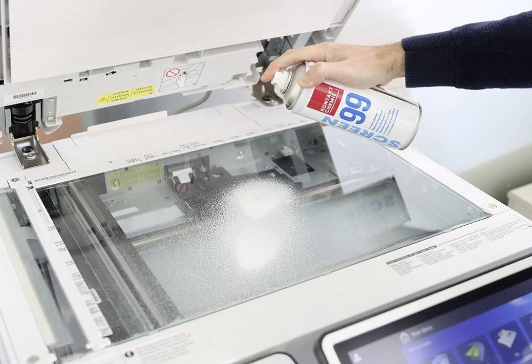 Un homme vaporise un liquide d'une bombe aérosol sur la surface vitrée d'un photocopieur pour le nettoyer ou l'entretenir.