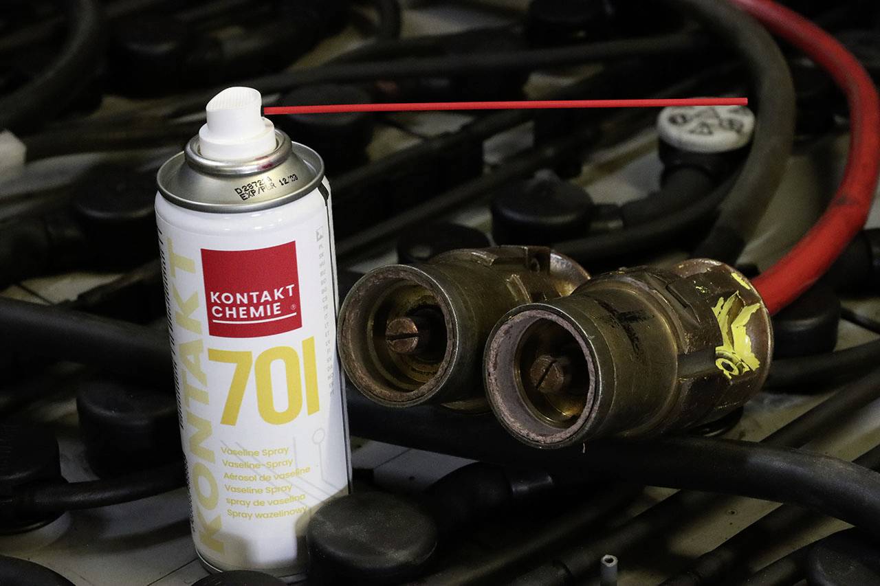 Une bombe aérosol portant l'inscription 'Kontakt Chemie 70' est posée à côté de deux grandes vannes métalliques. Des câbles sont visibles en arrière-plan.