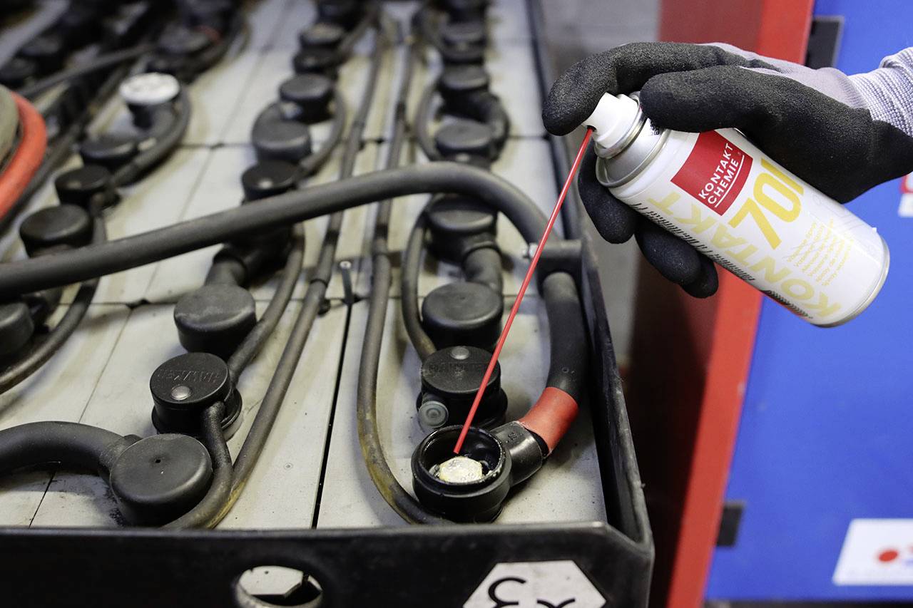 Une personne porte des gants et vaporise un produit de nettoyage à partir d'un aérosol sur la borne d'une batterie de voiture dans un atelier.