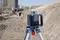 Un chantier avec un laser rotatif au premier plan sur un trépied. À l'arrière-plan, une personne mesure le terrain.