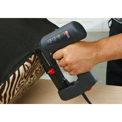 Une personne tient un agrafeur électrique et fixe un tissu noir sur un meuble au motif zébré.