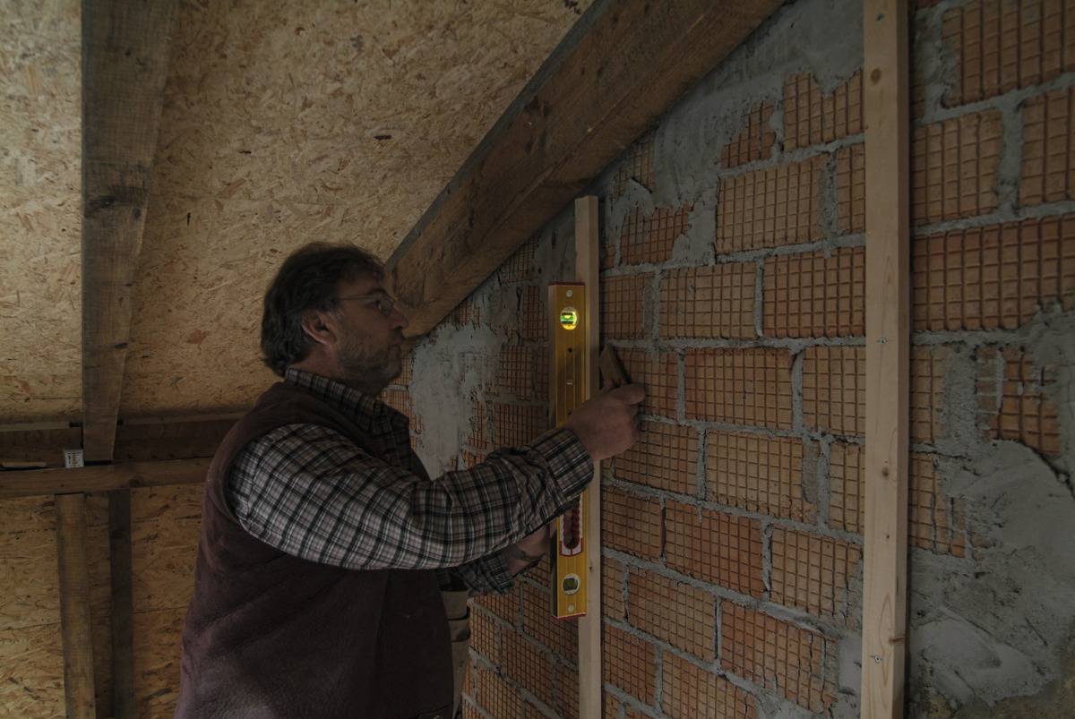 Un homme utilise un niveau à bulle et un crayon pour mesurer et aligner un mur de briques.