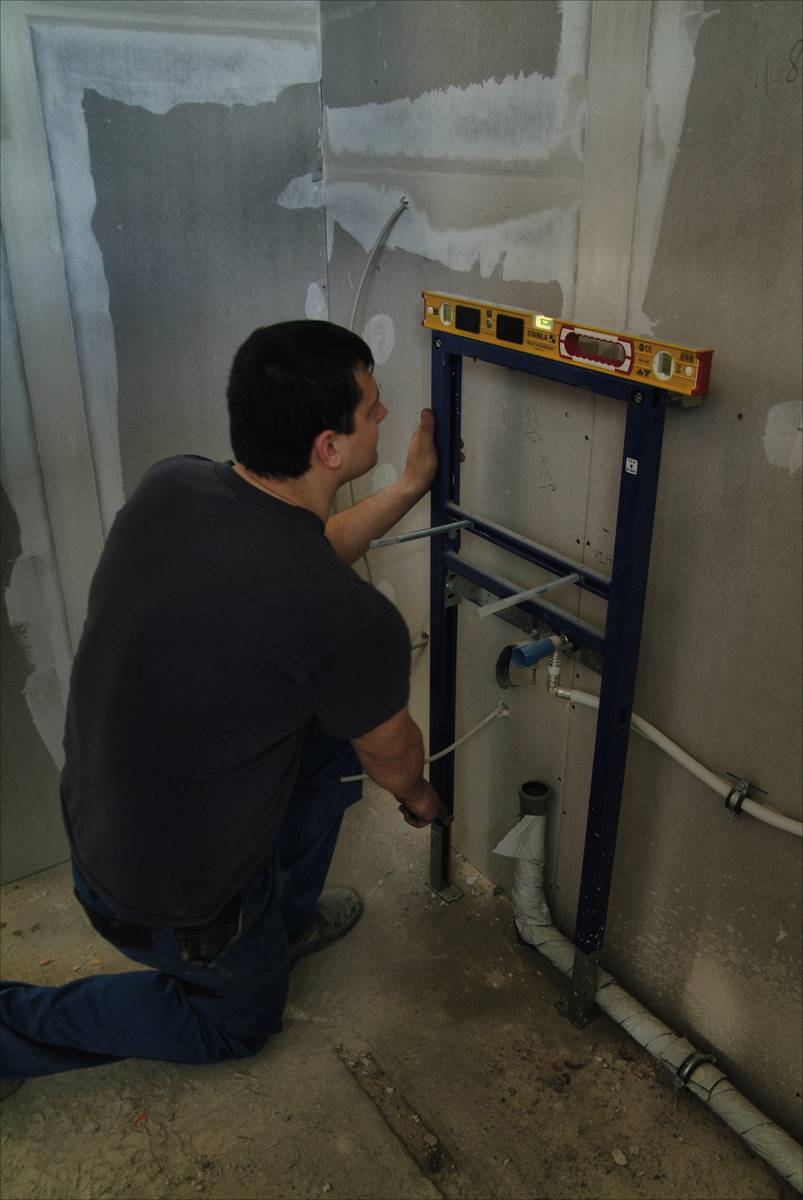 Une personne installe un support sanitaire sur un mur tout en vérifiant l'alignement à l'aide d'un niveau à bulle.