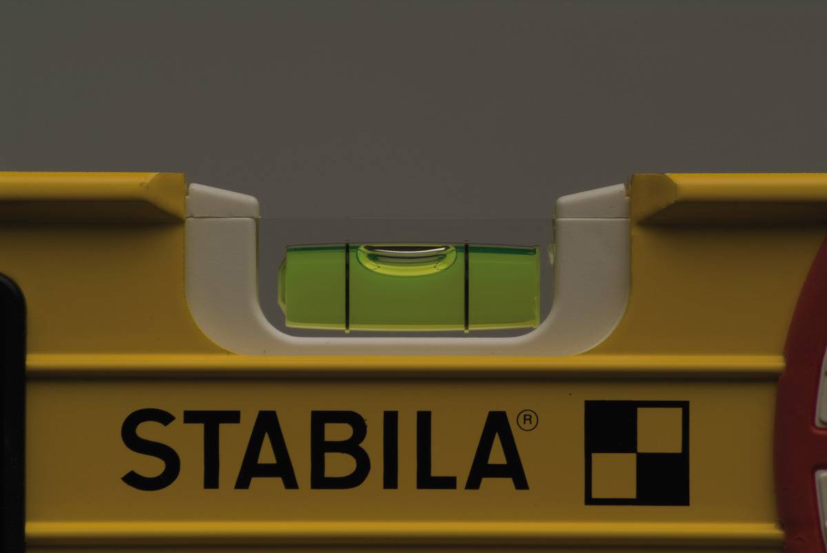 Niveau à bulle avec un boîtier jaune et une bulle verte centrée, sur un fond gris.