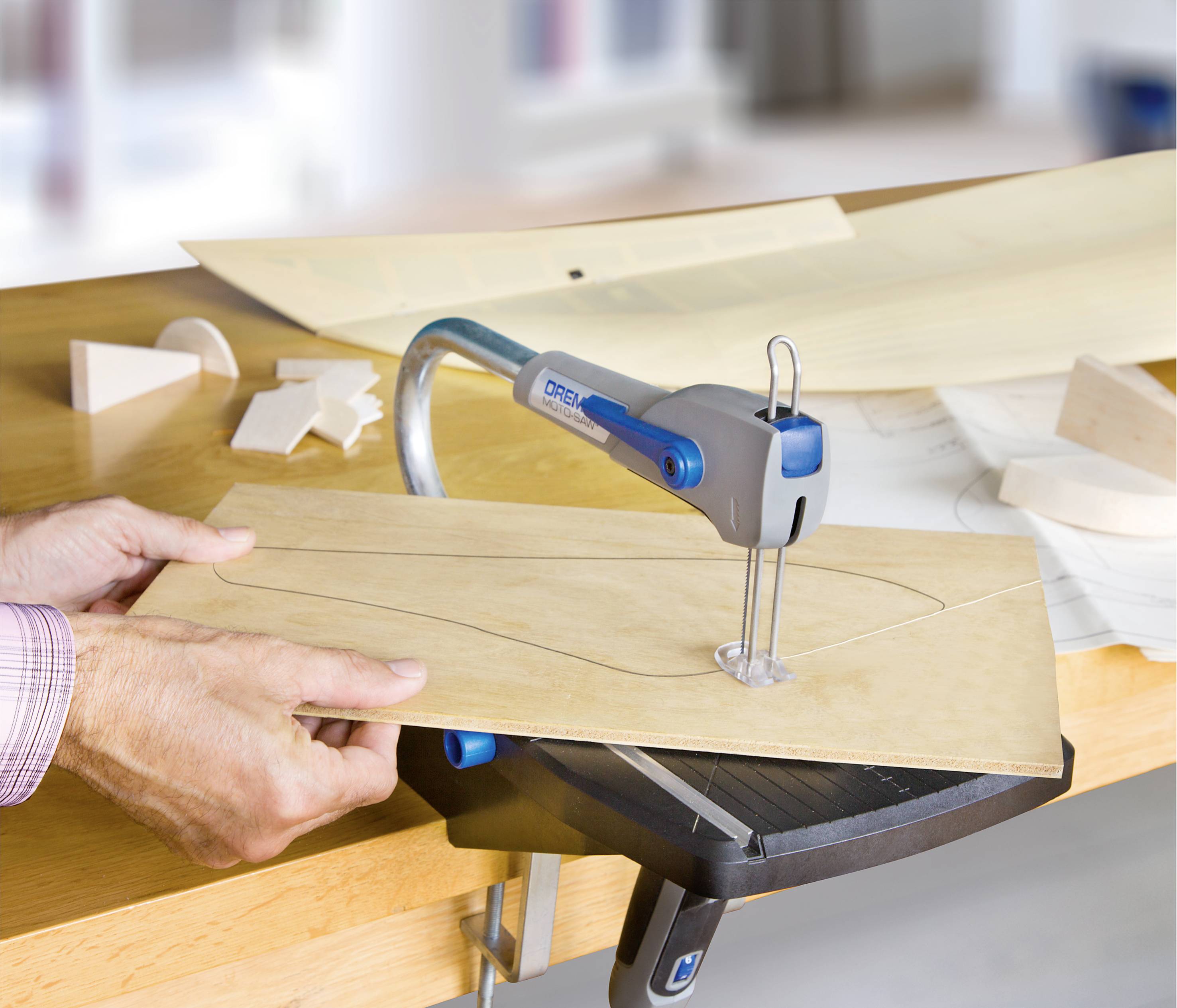 Une personne utilise une scie à découper pour découper une forme dans une fine planche de bois. D'autres pièces de bois sont posées sur la table.