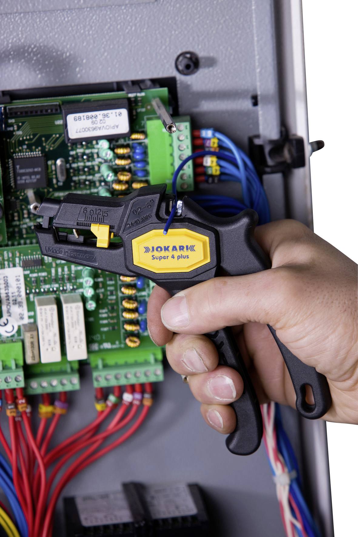 Un artisan utilise un outil Biokarx Super 4 Plus pour fixer des câbles dans un boîtier électrique, avec des circuits imprimés visibles.