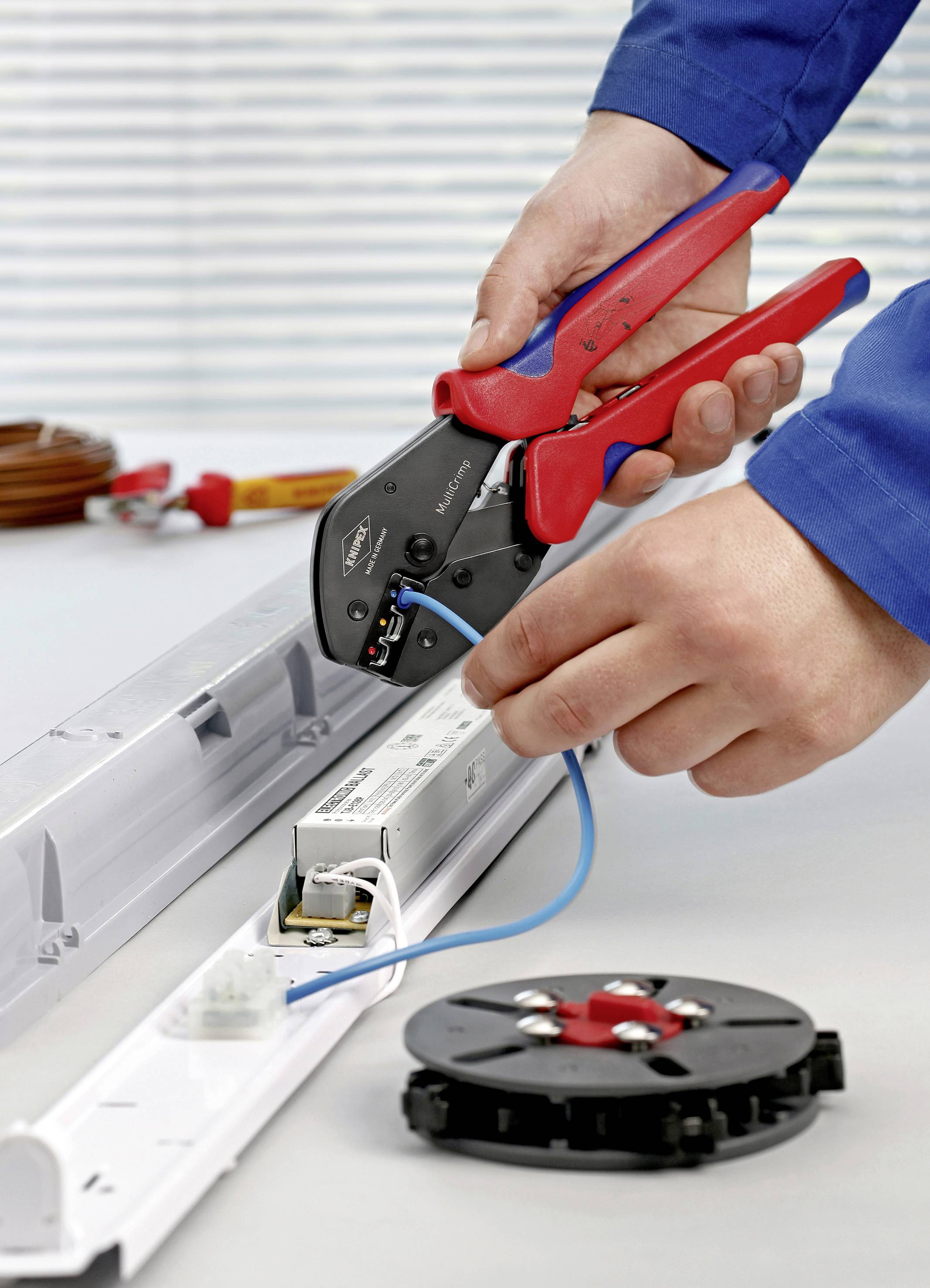 Une personne sertit une connexion électrique sur un luminaire LED à l'aide d'une pince à sertir sur une table de travail.