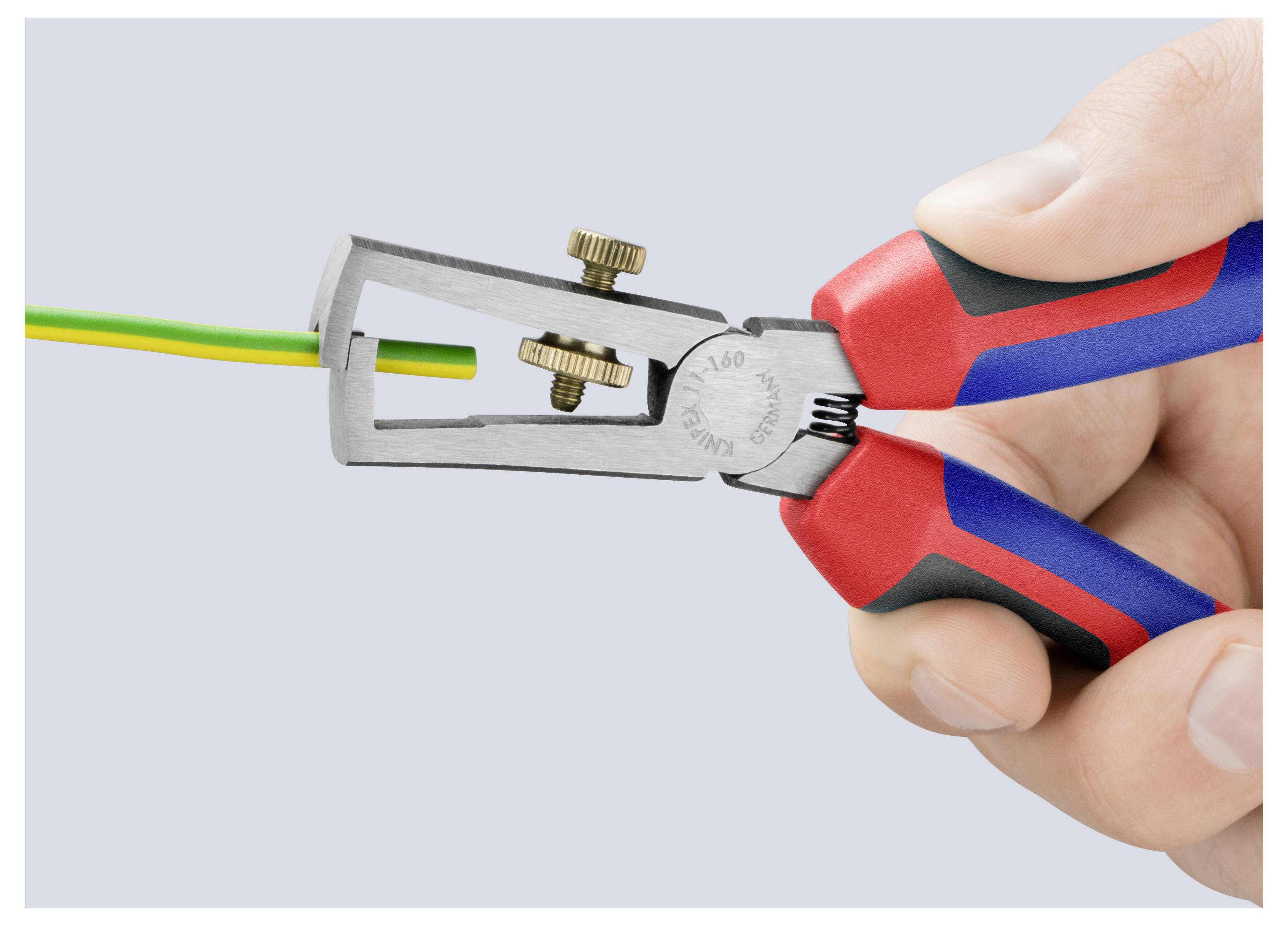 Main utilisant une dénudeuse pour enlever l'isolation d'un fil électrique jaune-vert.