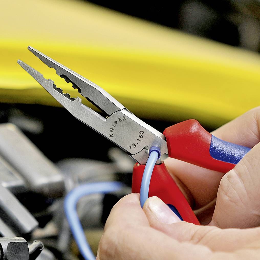 Une main tient une pince rouge qui dénude un câble bleu. Un objet jaune flou est visible en arrière-plan.