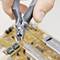 Une main tient un coupe-fil qui coupe un fil fin au-dessus d'un circuit électronique équipé de divers composants.