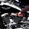 Une personne répare une moto avec une pince. Un moteur de moto chromé et un réservoir noir sont visibles.