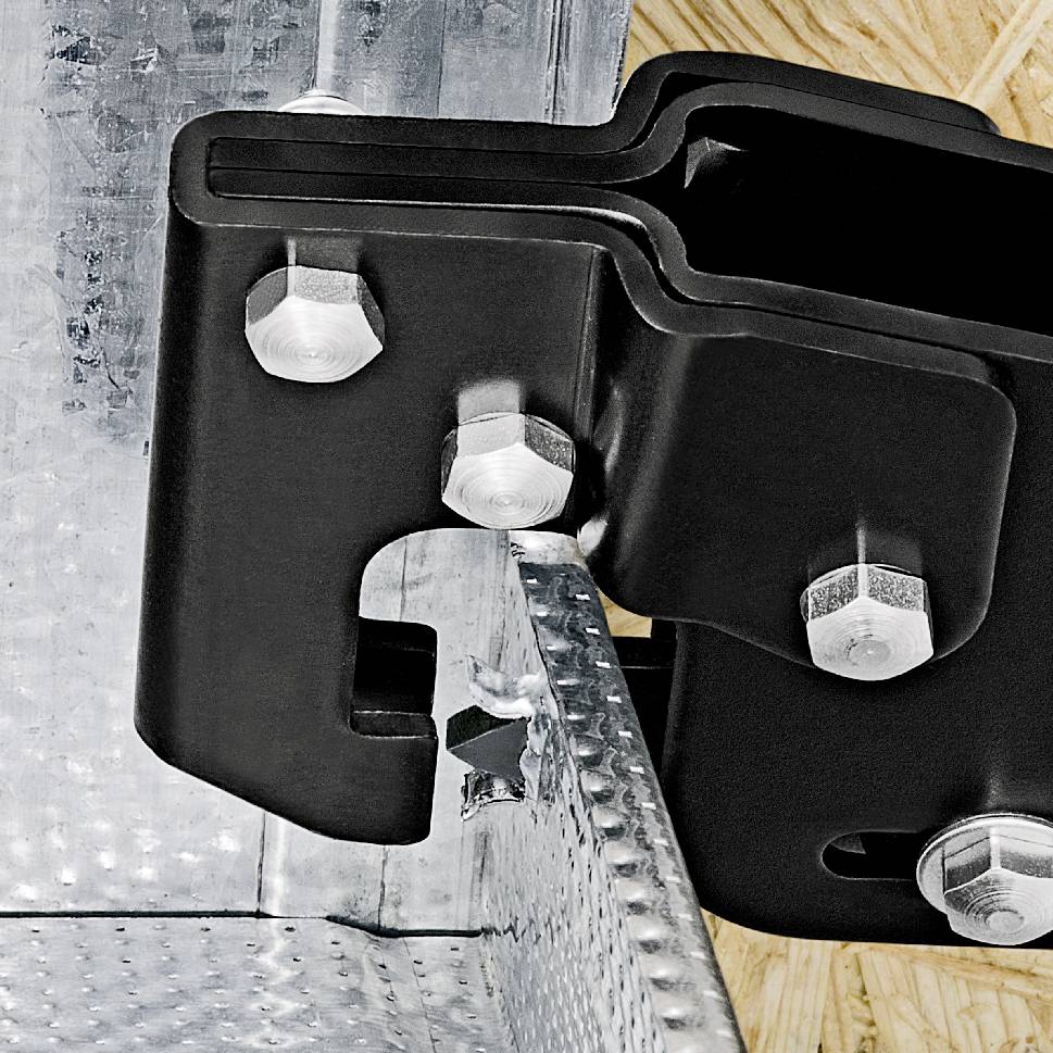 Un support noir en métal, fixé avec plusieurs boulons sur une surface argentée striée.