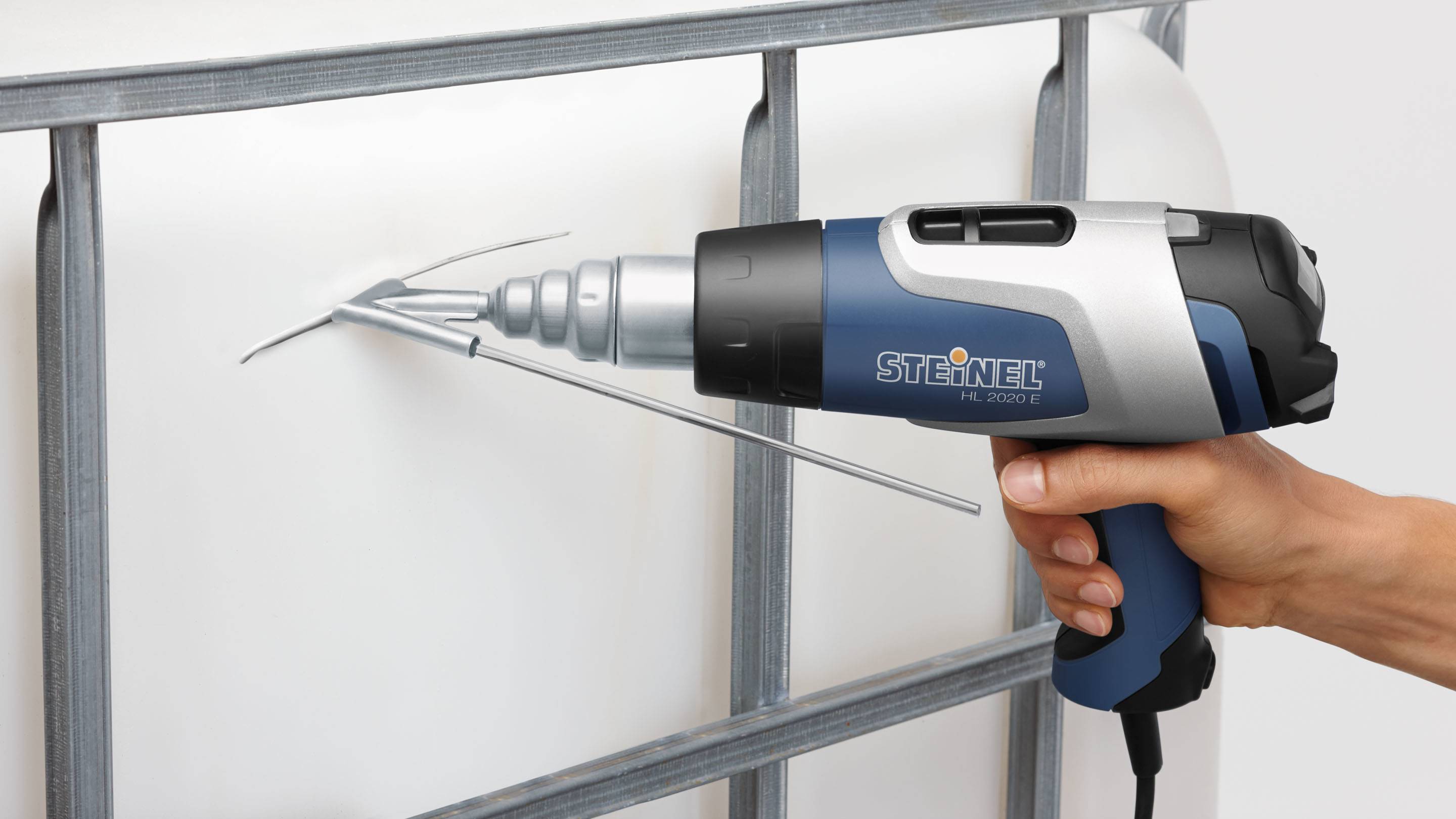 Une main tient un pistolet à air chaud qui coupe du plastique. L'appareil est bleu et noir et porte l'inscription 'Steinel'.