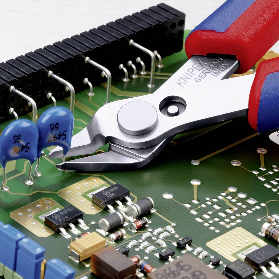 Un gros plan d'un circuit imprimé avec des composants électroniques, comprenant des condensateurs bleus et une pince multiprise prête à couper.