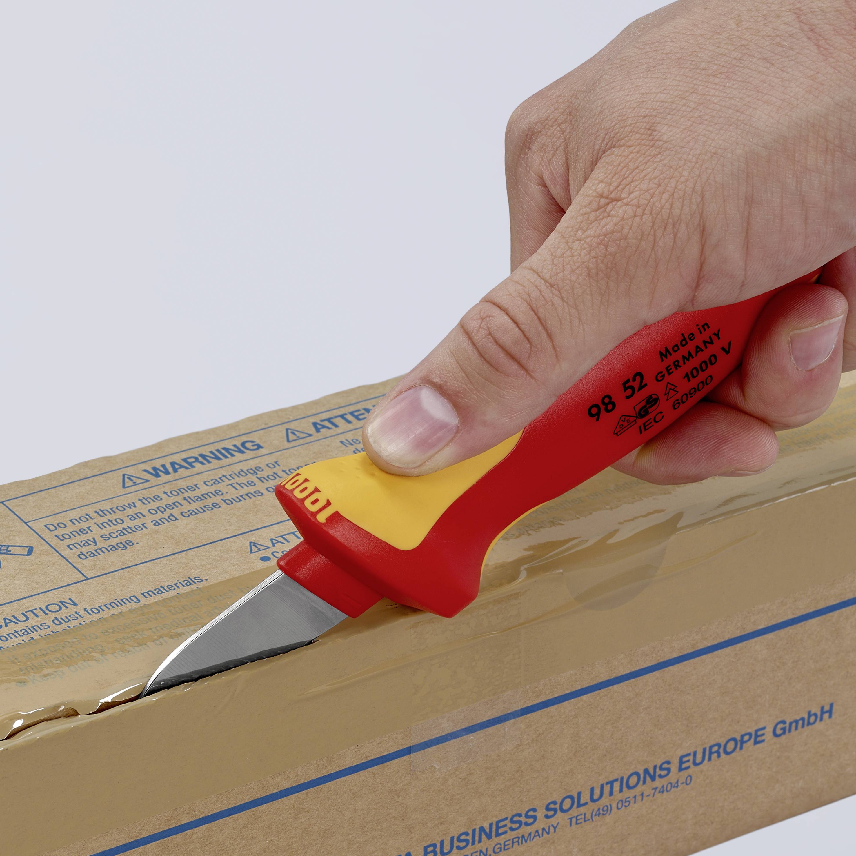 Une main coupe un carton avec un couteau de sécurité jaune. Le carton affiche l'adresse d'une entreprise en bas.