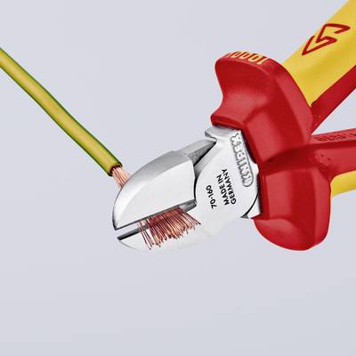 Une pince coupante VDE rouge et jaune coupe un câble vert et jaune, révélant de nombreux fils de cuivre.