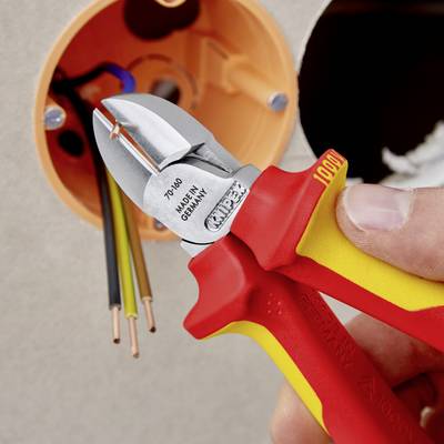 Gros plan d'une pince multifonction tenue dans la main droite, coupant un câble. Une prise électrique ouverte est visible en arrière-plan.