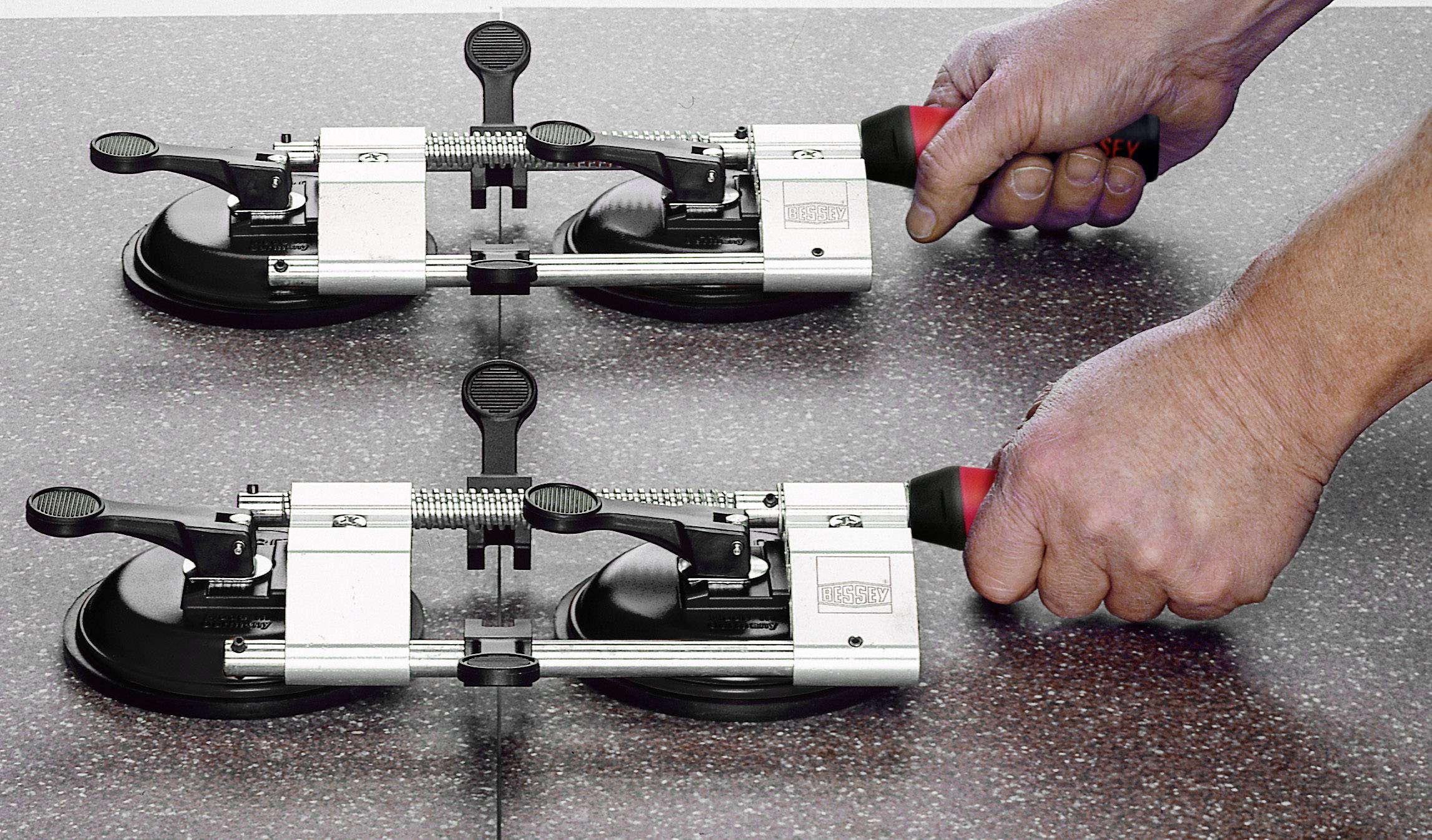 Deux mains tiennent des outils de pose de carrelage munis de ventouses, utilisés pour aligner correctement les carreaux sur une surface.