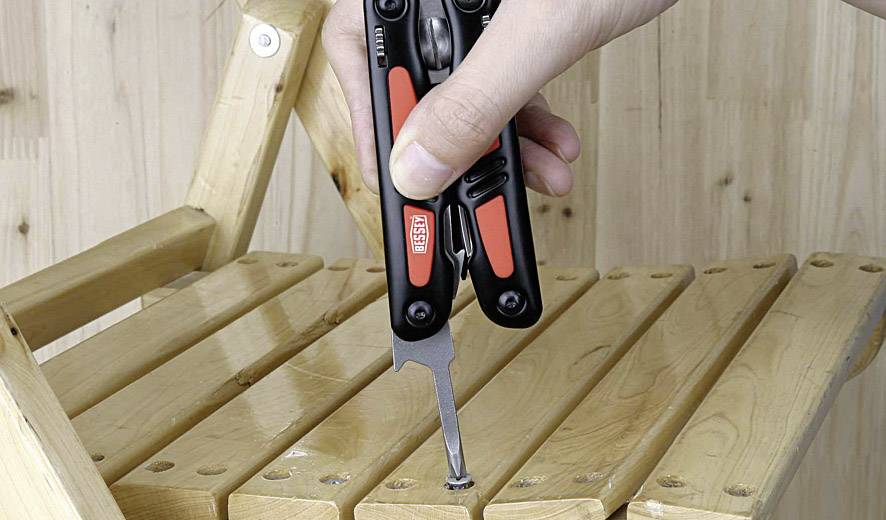 Une main utilise un outil multifonction noir et rouge pour serrer une vis dans un tabouret pliant en bois.