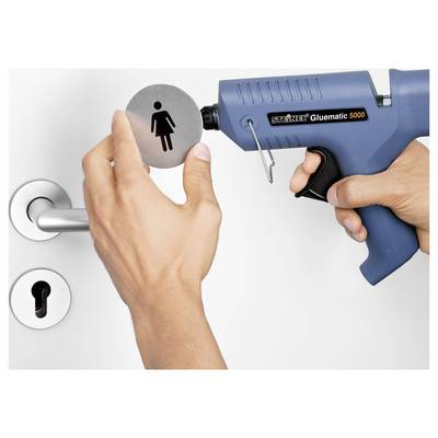 Une main utilisant un pistolet à colle thermofusible pour appliquer de la colle chaude sur une cheville en bois sur un plan de travail lors d'un projet d'artisanat ou de réparation.