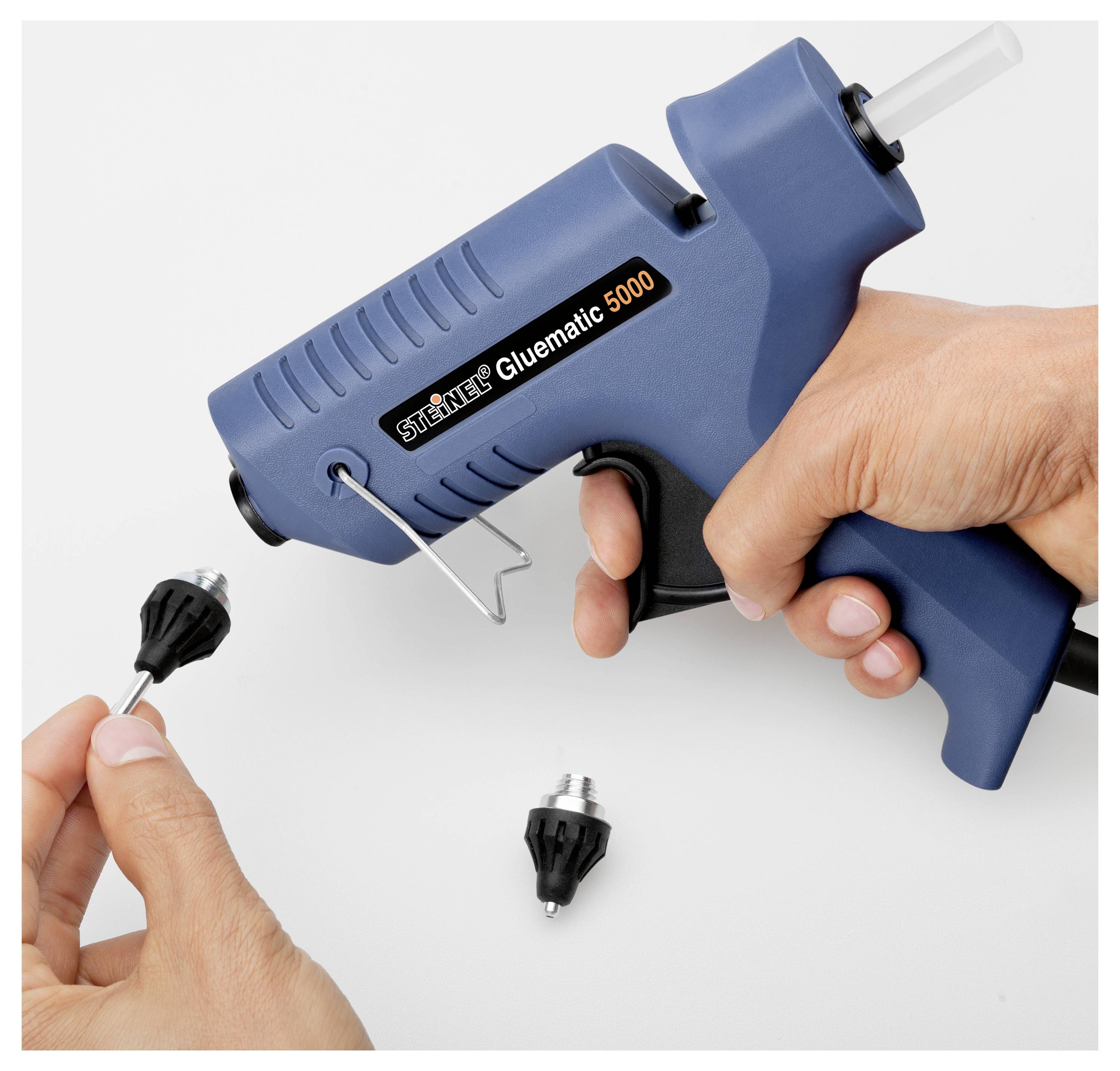 Des mains utilisant un pistolet à colle chaude bleu étiqueté « Steinel Gluematic 5000 » pour appliquer de la colle sur une petite buse noire sur une surface blanche.