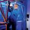 Un homme en tenue de protection et lunettes de sécurité tient un tube à essai dans un environnement industriel éclairé par une lumière bleue.