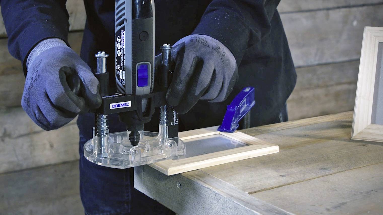Une personne utilise une défonceuse pour travailler un cadre rectangulaire en bois sur une table en bois.