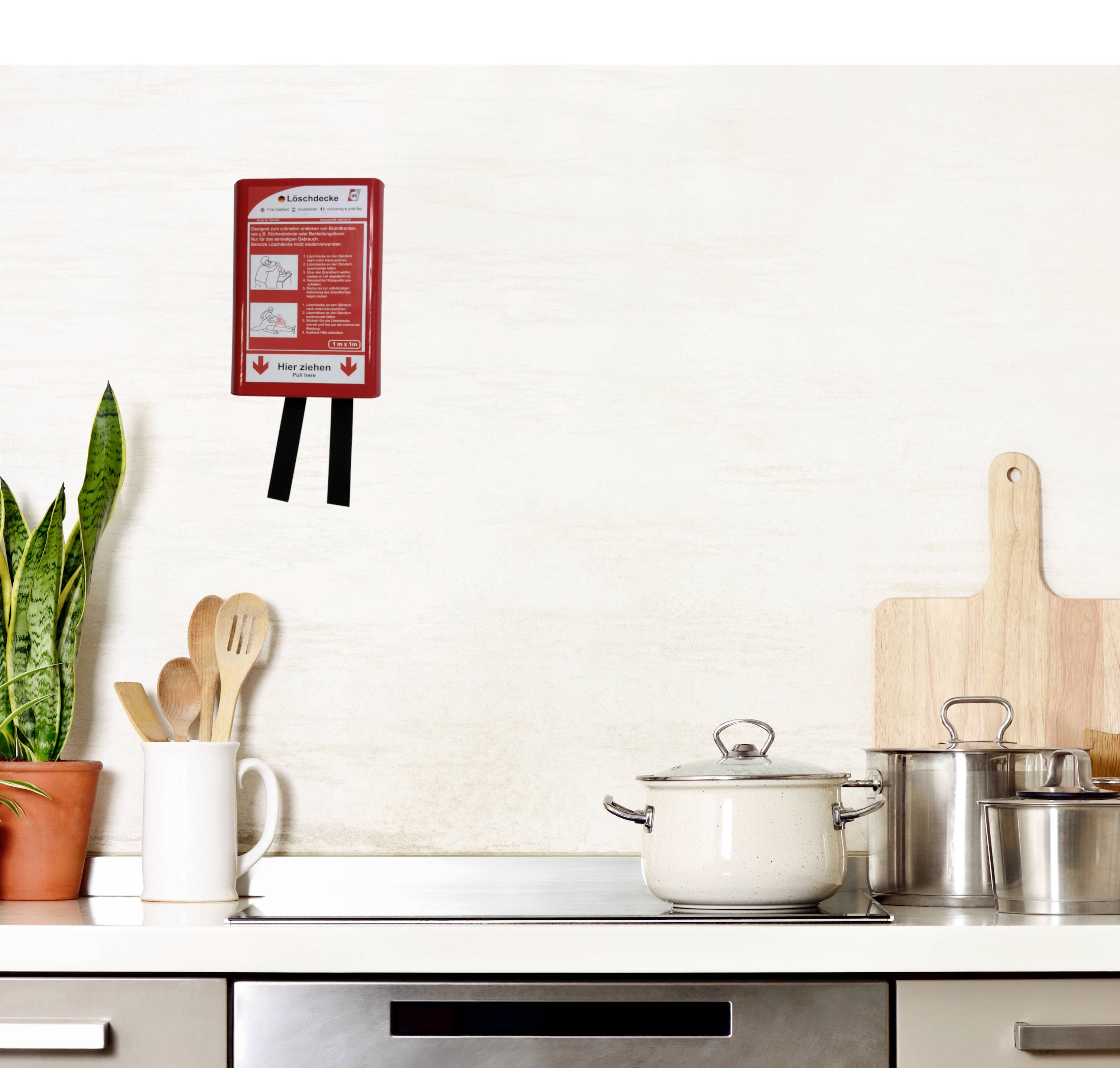 Cuisine beige avec une casserole blanche sur la cuisinière. Un panneau rouge avec des instructions est accroché au mur. À gauche, une plante est placée dans un pot.