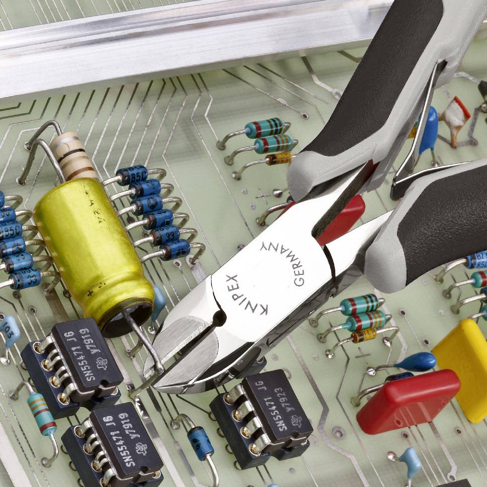 Carte électronique avec résistances, condensateurs et circuits intégrés. Une pince touche l'un des circuits.